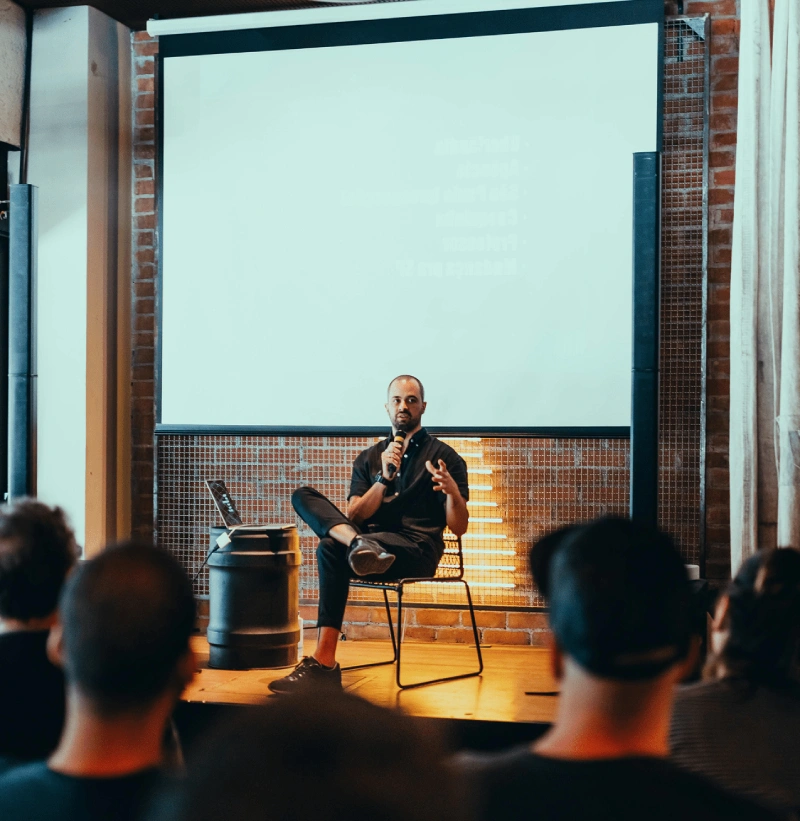 A man sitting on top of a chair in front of a projector screen.